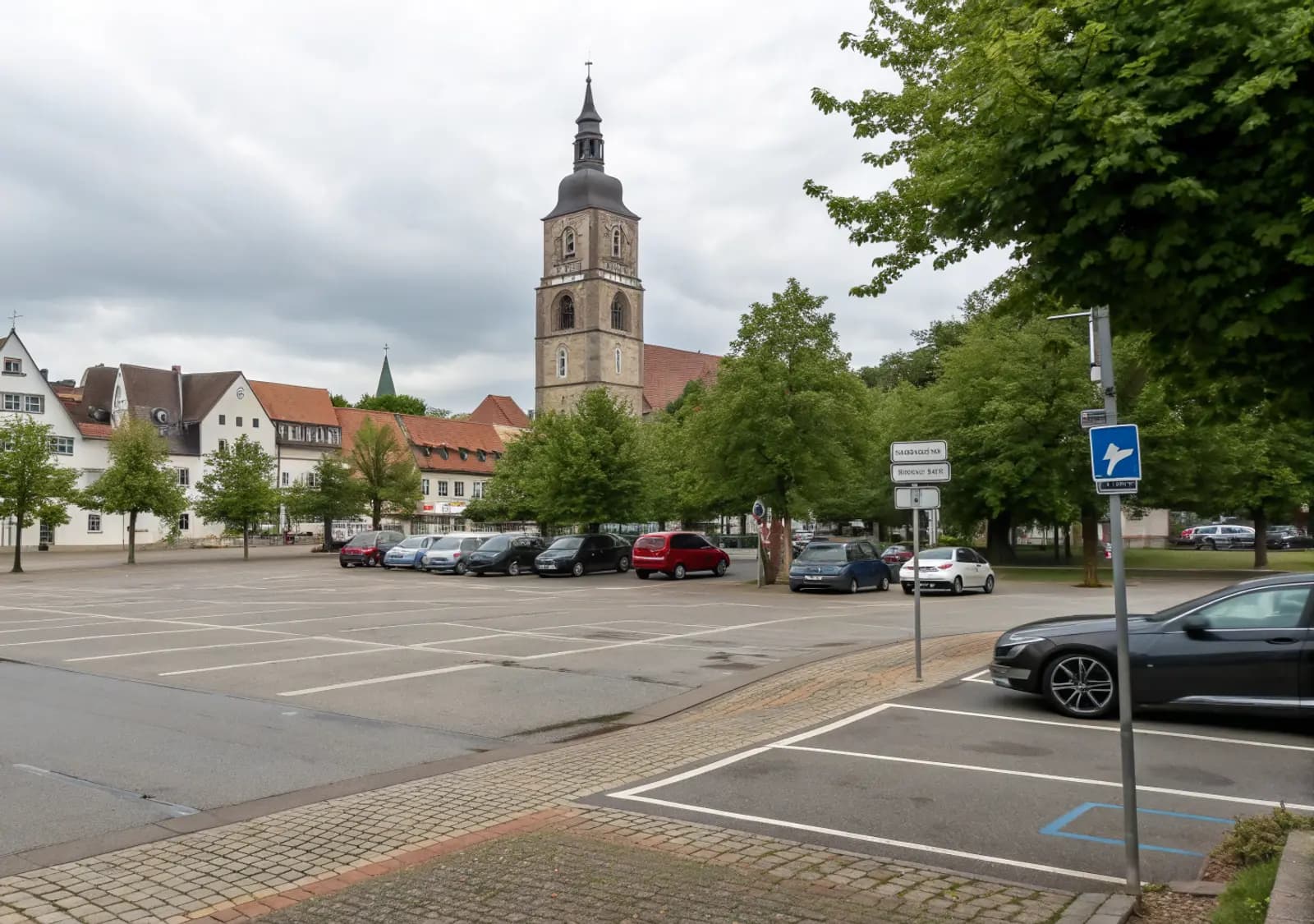 Öffentlicher Parkplatz am Rand einer Innenstadt mit Kirchturm (illustrative Szene)